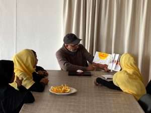 reading a book to a group of girls, plate of oranges in front